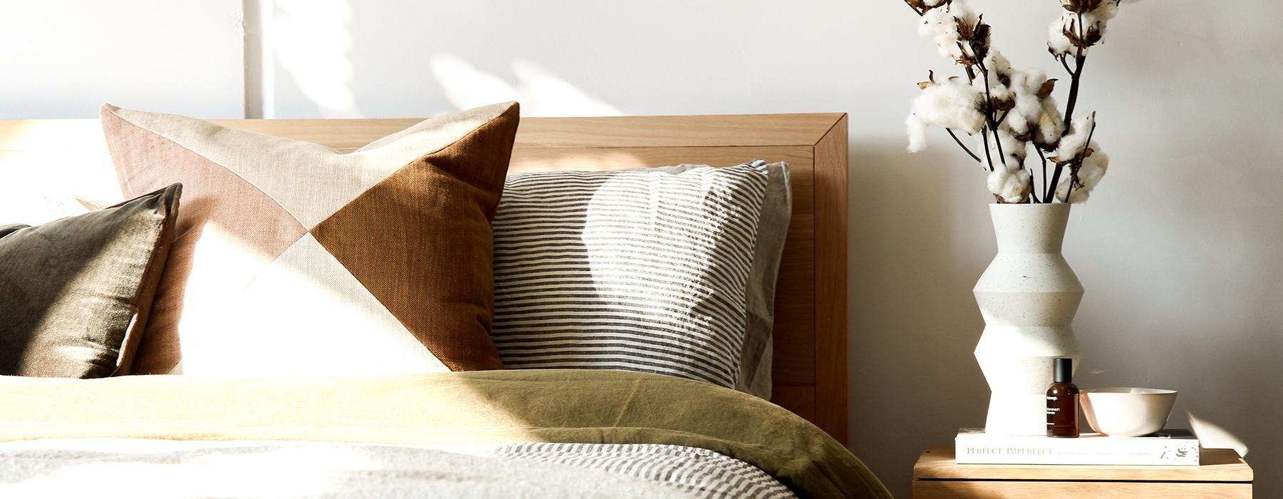 nightstand with a vase of cotton stems next to bed